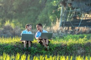 Two young boys sitting in a field with laptops.