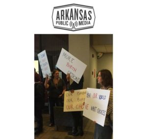 A group of people holding signs in front of the arkansas public broadcasting logo.